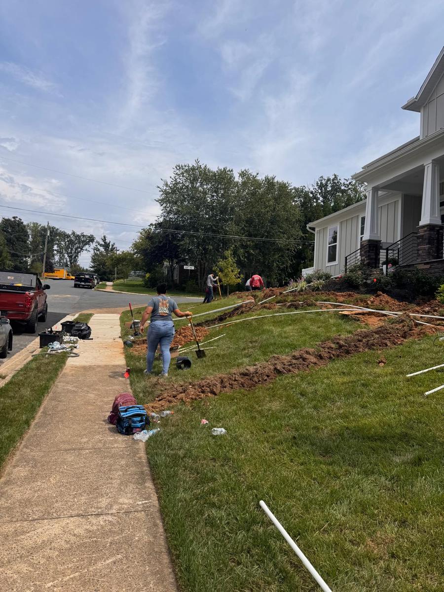 Crew trenching a front yard along the sidewalk beside a light-gray home