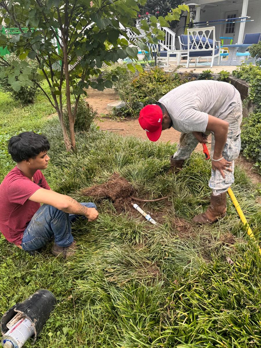 Technicians inspecting a sprinkler head repair in a shaded garden bed