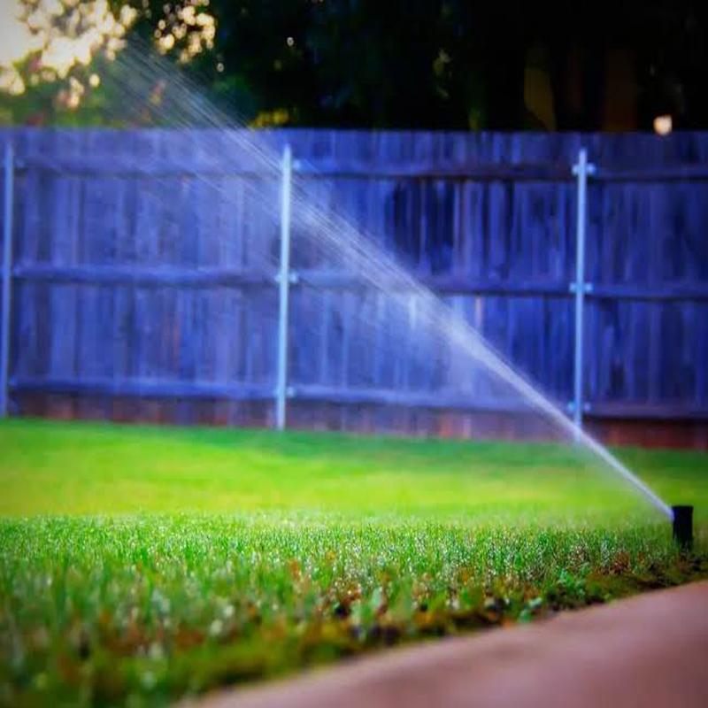 Lawn and fence line at dusk with irrigation running